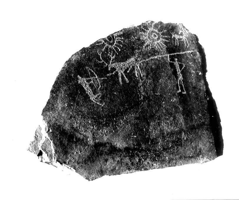 A photograph of a carved limestone slab from Burzahom, showing a stag, hunters, a dog, and two solar discs in the upper register
